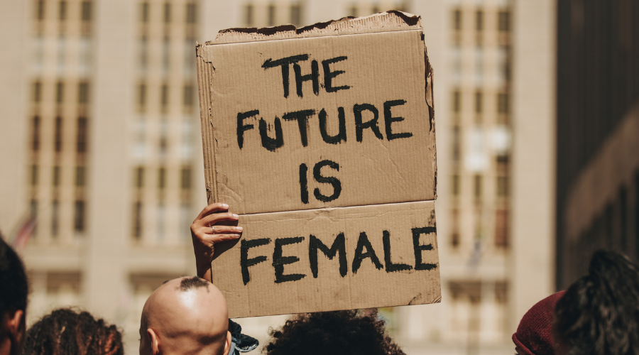 hand holding a cardboard poster with "the future is female" written in black marker